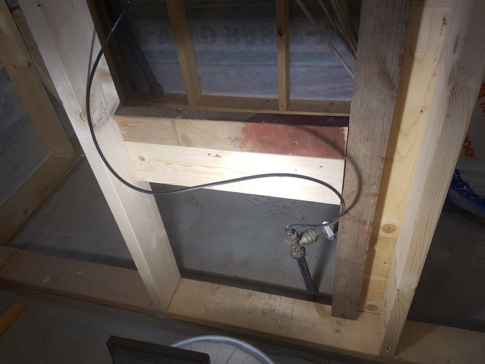 Värmekabel installerad i ett vattenrör i en timrad konstruktion, väntar på att anslutas till strömkälla.