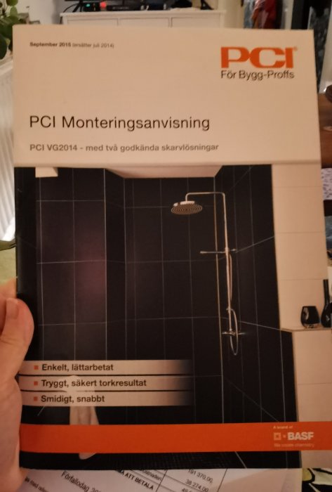 Hand håller en PCI monteringsanvisning för duschtillbehör med bild och fördelar listade.