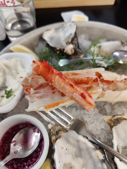 Skivade crabsticks i förgrunden med ostron och tillbehör i bakgrunden på isbädd.