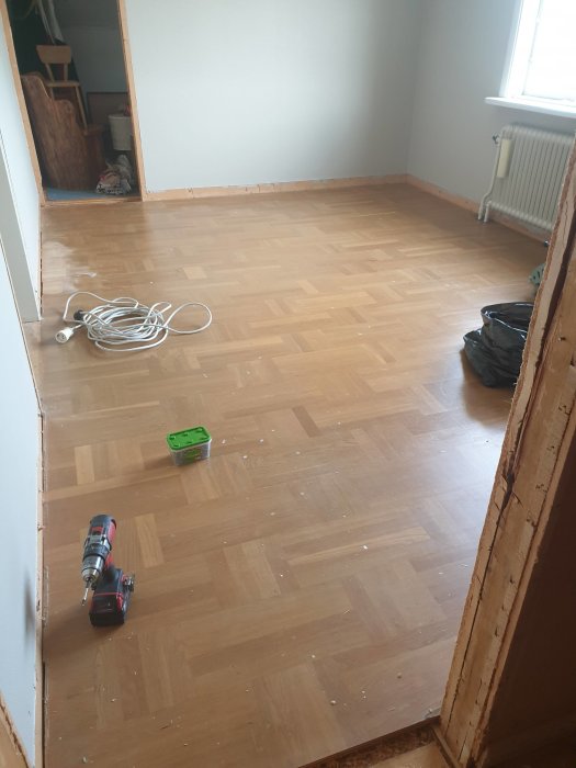 Oslipat parkettgolv i ett rum med elverktyg och kabel på golvet.