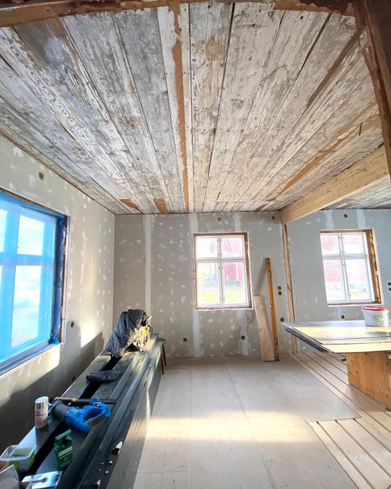 Ett ruffigt innertak med flagnande färg i ett halvrenoverat kök, med byggmaterial och verktyg synliga.