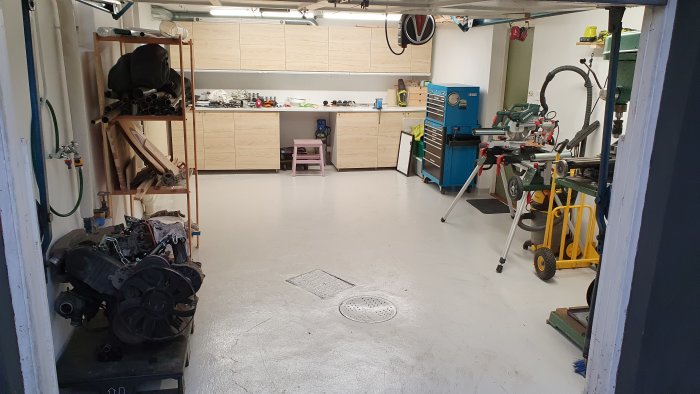 Uppstädad garageinteriör med arbetsbänkar, verktyg och en delvis demonterad motor på ett stativ, redo för bilens ankomst.