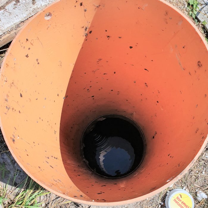 Öppning av orange trekammarbrunn med vatten i botten och reflektioner från himlen, utan synliga kammare.