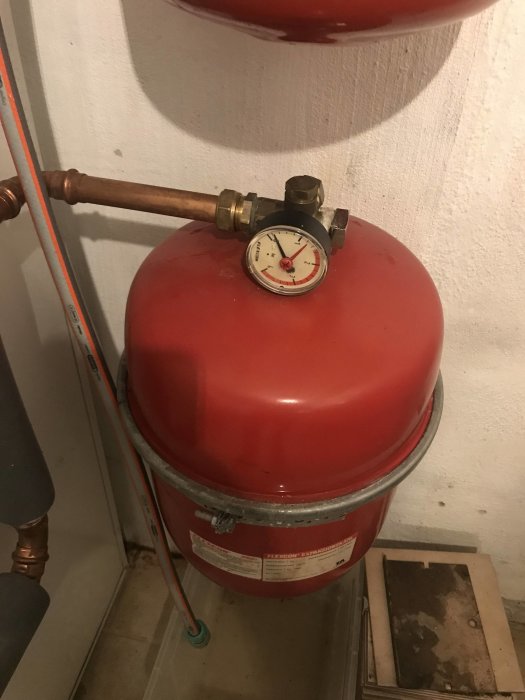 Expansionskärl med manometer och ratt i ett pannrum, indikerar trycknivån i systemet.