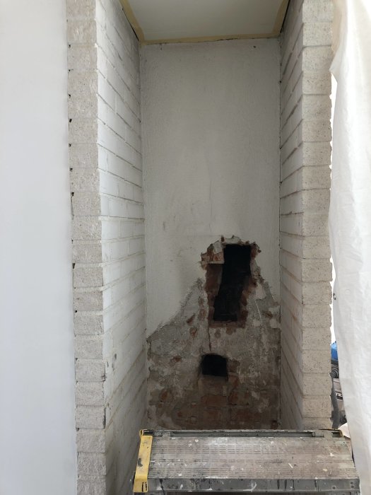 Putsad öppen spisnisch med synlig murad öppning i en vitmålad hall, redo för installation av antingen insats eller smalspis.