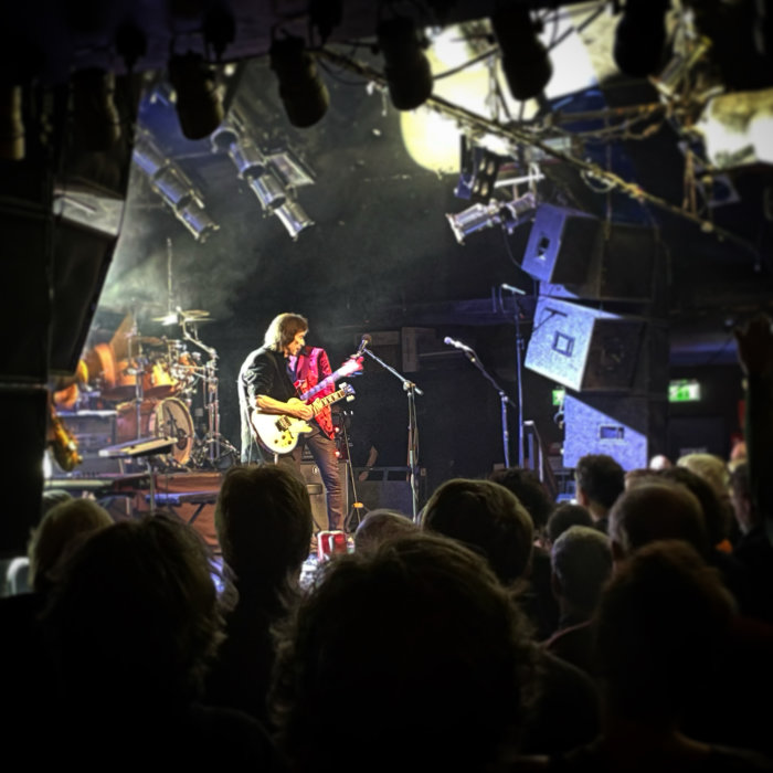 Gitarrist spelar live på scen inför publik i en intim konsertlokal.
