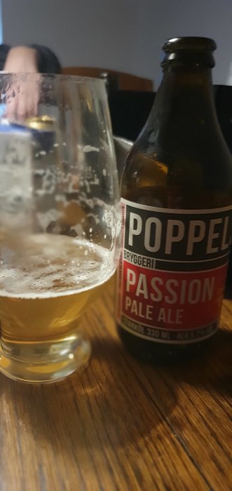 En halvfull ölglas och en flaska Poppels Passion Pale Ale på ett bord.