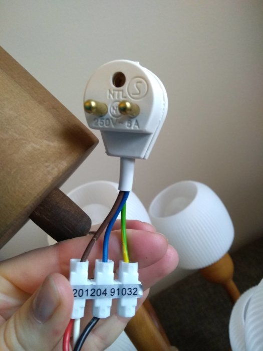 Hand håller en vit elektrisk stickkontakt med blå och brun kabel ansluten via kopplingsklämmor, säkringen gick fel.