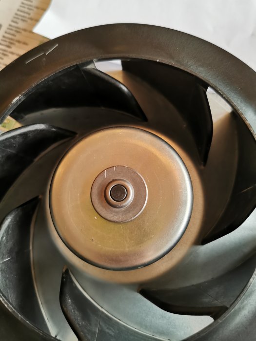 Närbild av en fläktbladsturbin med borttagen låsring, visar central axel och svarta blad mot en grå bakgrund.