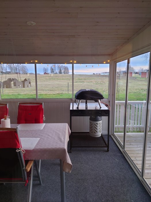 Uteplats med pizzaugn på bord, bord med duk, stolar och utsikt över landskap.