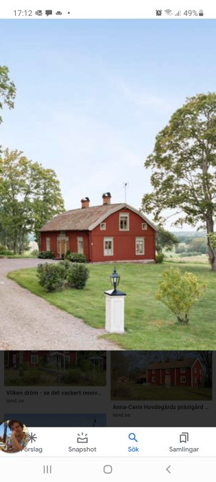 Röd trästuga med vita knutar och två skorstenar i lantlig miljö, omgiven av grönt gräs och en grusväg.