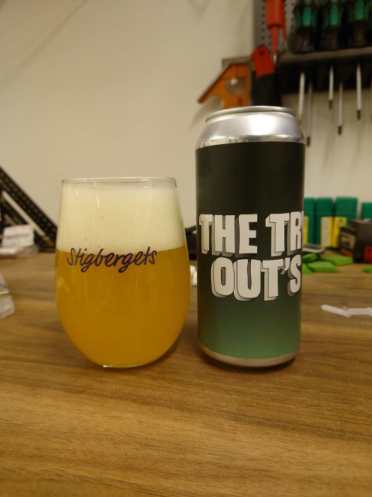Ölglas fyllt med gul vätska bredvid en burk med texten "THE TROUT'S" på ett verktygsbord.