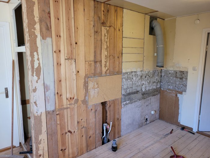 Vägg med halv plank och halv putsad murstock efter köksrivning, redo för renovering.