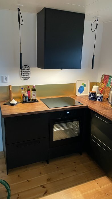 Ny bänkskiva i kök med svarta skåp, inbyggd ugn och trägolv.