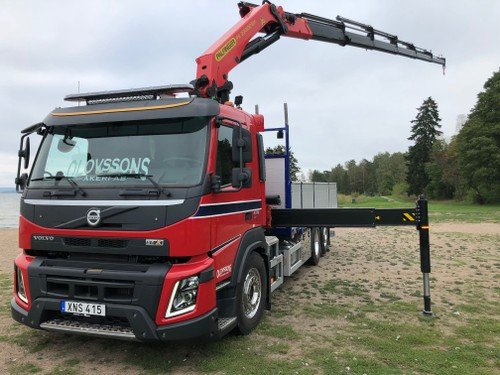 Kranbil parkerad på gräs med utfällda stödben och kranarmen utsträckt åt sidan.