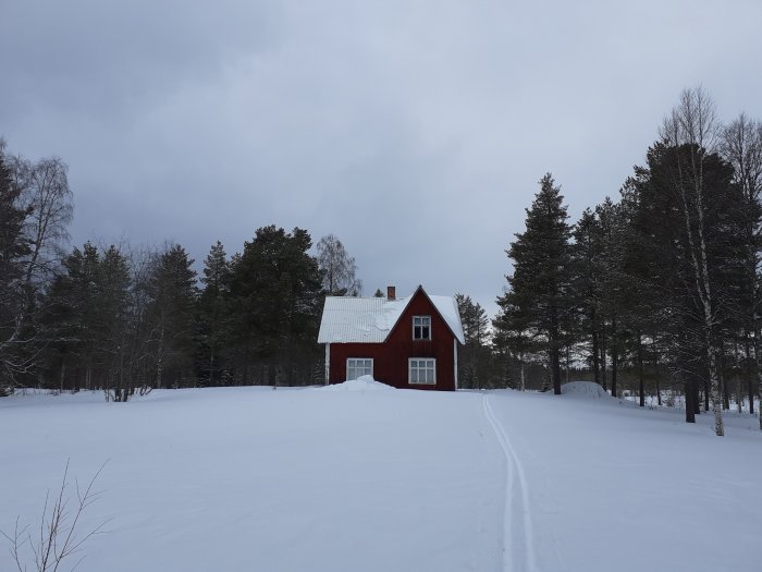 Rödfärgat charmigt hus från 1919 med snötäckt fasad omgiven av snö och skog.