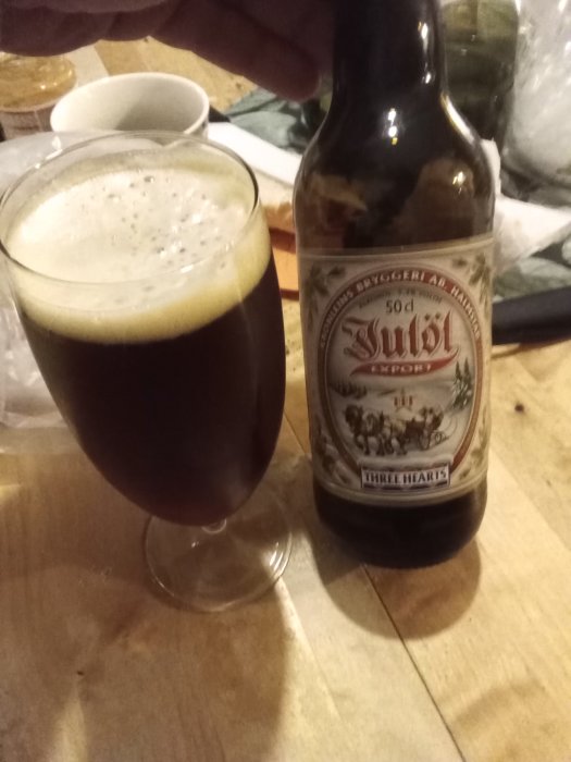 Ett glas mörkt öl och en ölflaska på ett bord, som tyder på en kylig och mysig kväll inomhus.