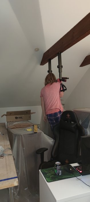 Renoveringsarbete i hemmamiljö med synliga takbjälkar och en person som monterar utrustning vid en arbetsstation.