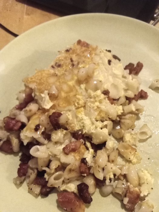 En tallrik med makaronipudding toppad med knaperstekt sidfläsk, serverad på ett köksbord.