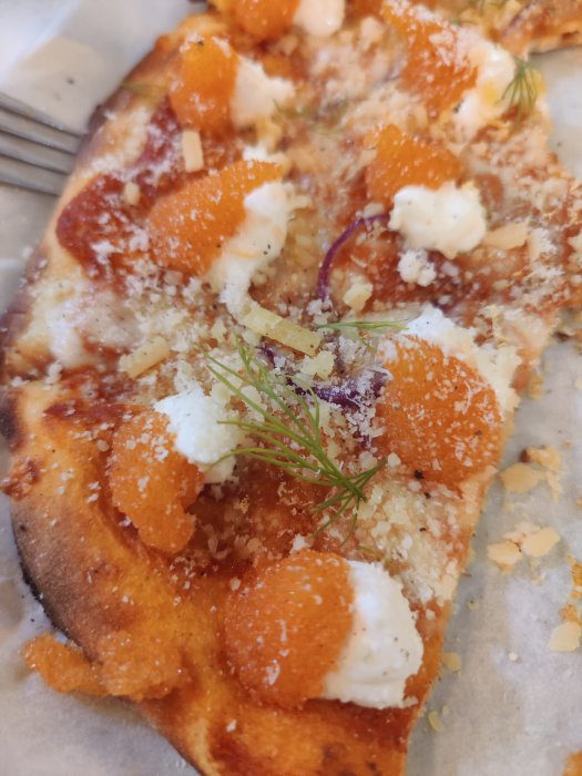 En bit löjromspizza med rikligt med löjrom, färskost och dill på ett bakplåtspapper.
