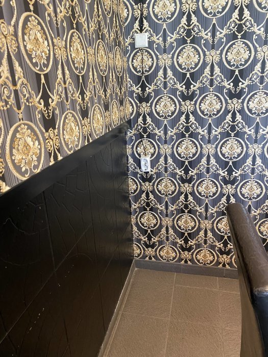 Ornate wallpaper with a visible electrical outlet and cord in a restaurant setting.