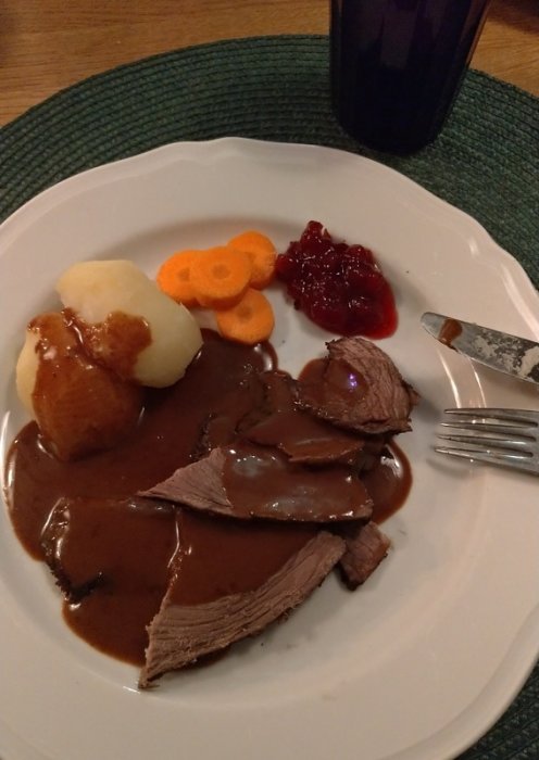 Porterstek på tallrik med potatis, morot, lingonsylt och sås, bredvid en kniv och gaffel.