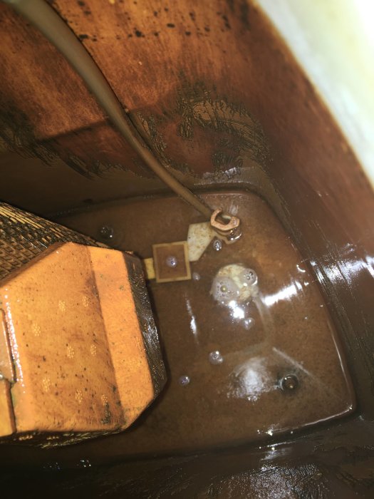 Inre delen av en IFÖ toalett med järnhaltigt och smutsigt vatten samt avlagringar.