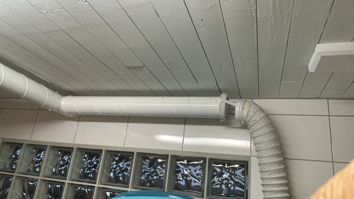 Nytt FTX-system i tak, synliga vita ventilationsrör mot en trätak bakgrund och glasblocks vägg.