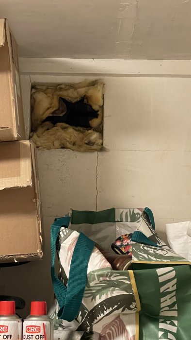 Ett öppet ventilationshål i källarvägg med synlig isolering och omgivna föremål.