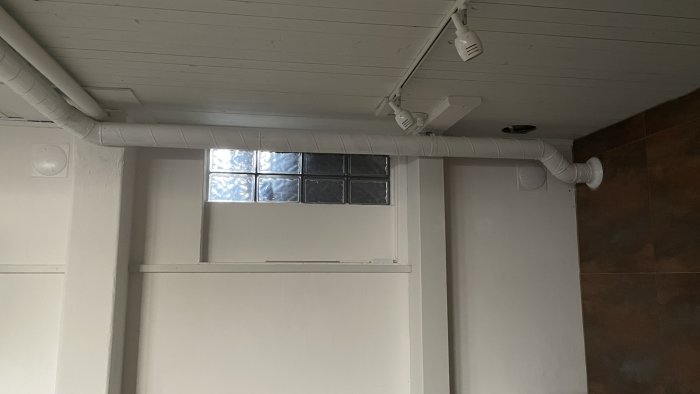 Nytt FTX-ventilationssystem installerat längs taket i ett källarrum med blockfönster.