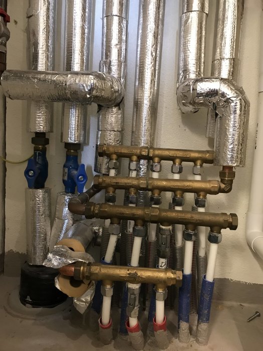 Isolerade VVS-rör och en fördelare för värmesystemet i ett värmerum, med synliga ventiler och anslutningar.