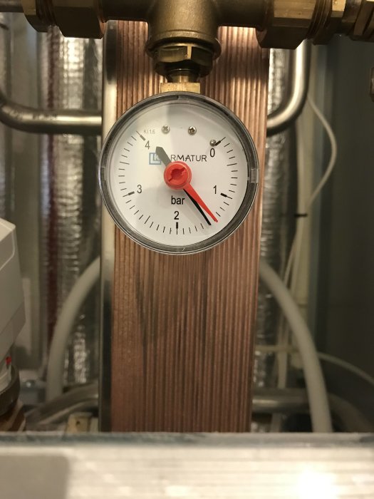 Manometer på fjärrvärmesystem som visar trycket i bar, omgiven av rör och ventiler.