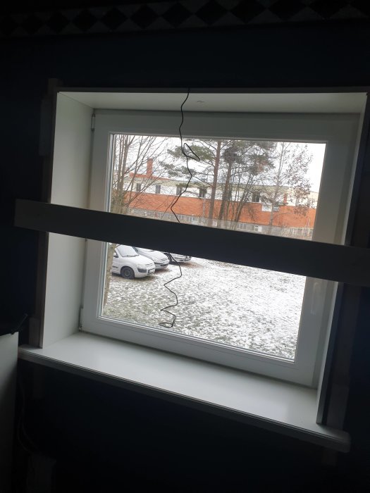 Nyinstallerad vit fönsterbänk med en lampa och kablar på, och en träregel tvärs över fönstret.