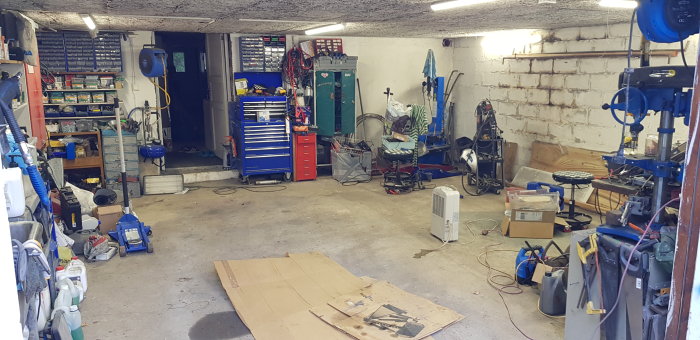 Ett tomt garage med spår av renovering, verktyg och utrustning utspridda på golvet.