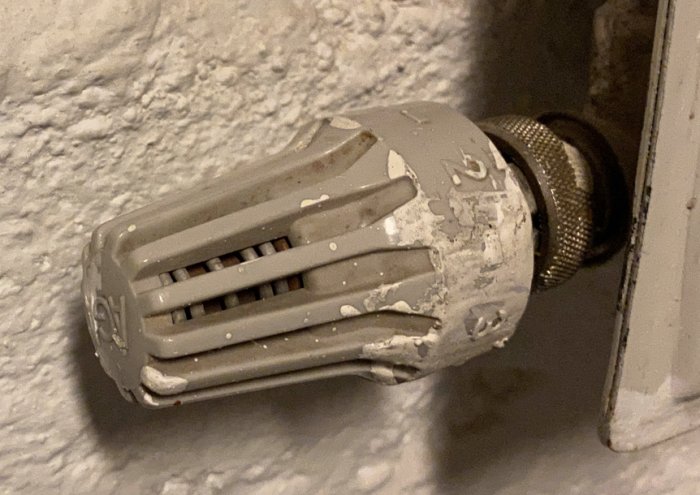 Äldre radiatortermostat med flagande färg som är fäst på en radiator.