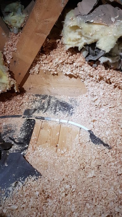 Bild av ett hål i ett vävspänt tak som visar strukturerna ovanför, täckt av spån och isoleringsmaterial.