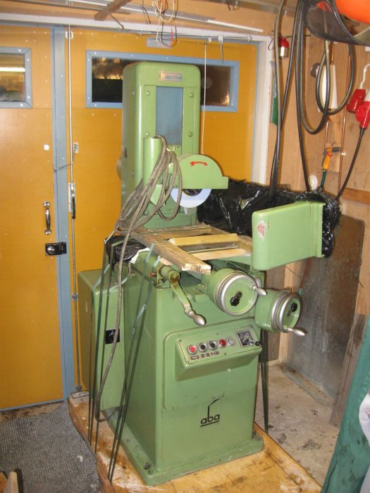 Industriell verkstadsmaskin inplastad inuti en verkstad med verktyg och kablar runtomkring.