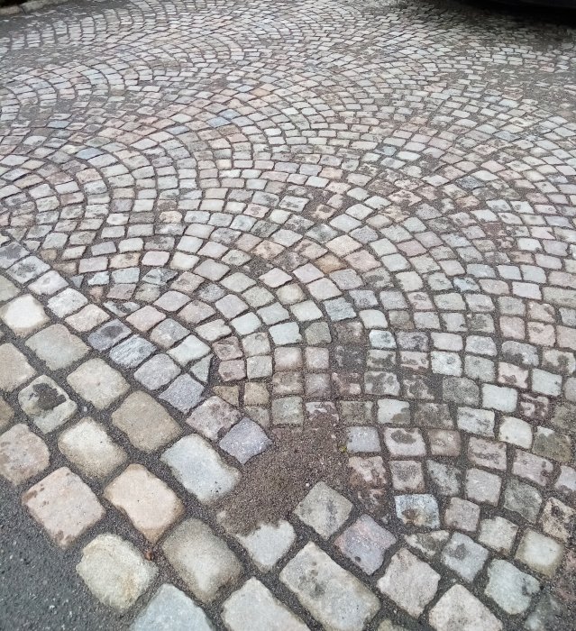 Gamla handhuggna granitgatstenar från 1800-talet, lagda i ett mönster på en gata.