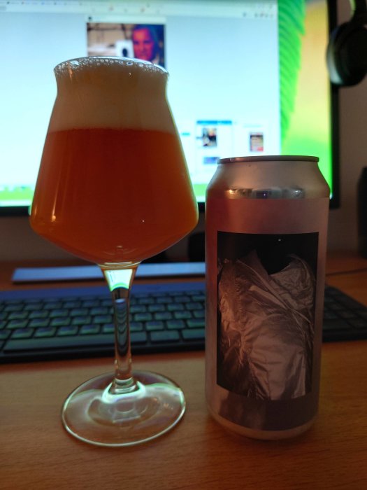 Ett ölglas fyllt med skummande öl och en ölburk framför en datorskärm.