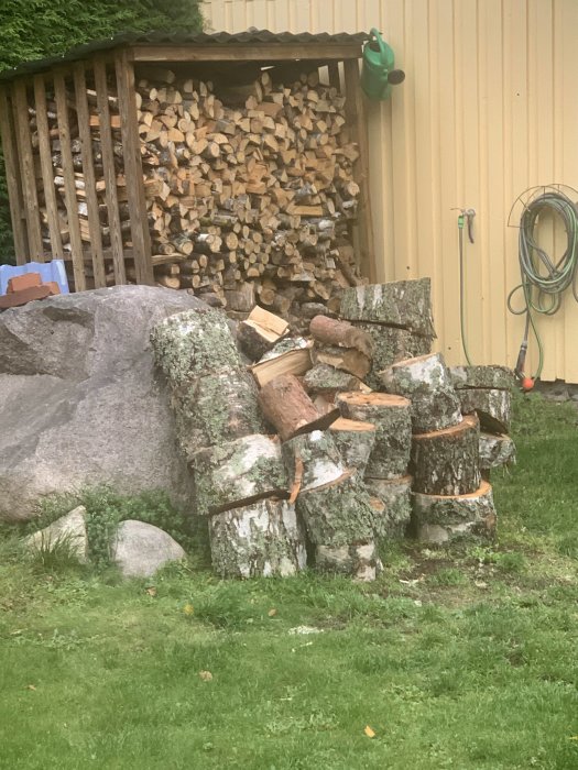 Vedstapel i en trädgård framför ett vedskjul, indikerar förberedelser för en varm kamin och lägre elförbrukning.