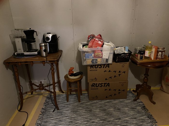 Provisoriskt kök med kaffebryggare och airfryer på gammalt bord, lådor och matvaror under renovering.