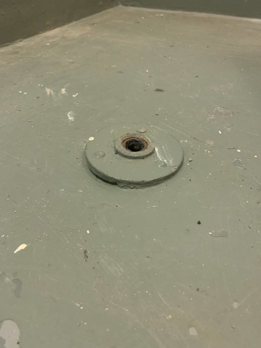 Metallföremål inmurat i betonggolv, ser ut som en gammal fixtur eller plugg.