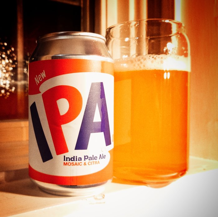 Burk och glas med IPA-öl på ett bord med svagt bakgrundsljus.