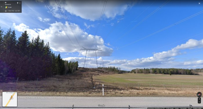 Vy över landskap med kraftledningsstolpar, träd och en väg under molnig himmel.