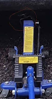 Blå hydraulisk domkraft med säkerhetsvarningar synlig från ovansidan på grusig mark.