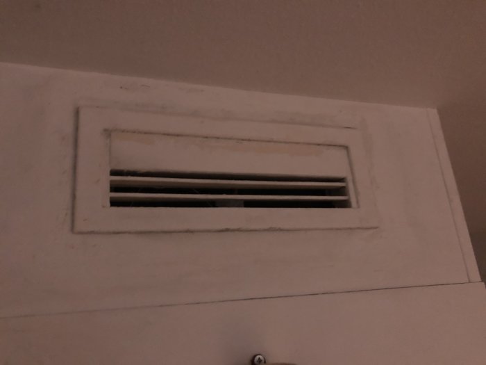 Vit rektangulär ventilationsdon monterad högt upp på en vägg i en lägenhet.