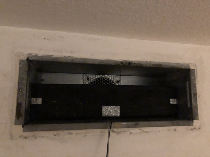 Ett öppet ventilationstilluftsdon i en vägg med synliga ventilationsrör och isoleringsmaterial.