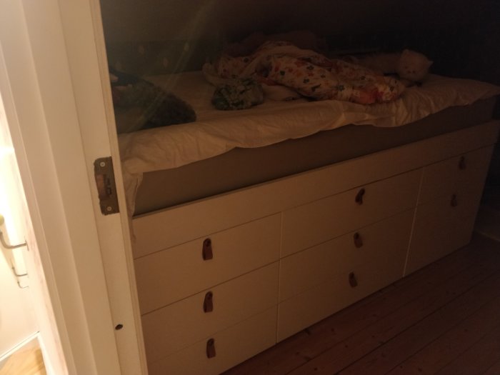 Dotterns säng byggd ovanpå vita Ikea köksskåp och reglar med lakan och gosedjur.