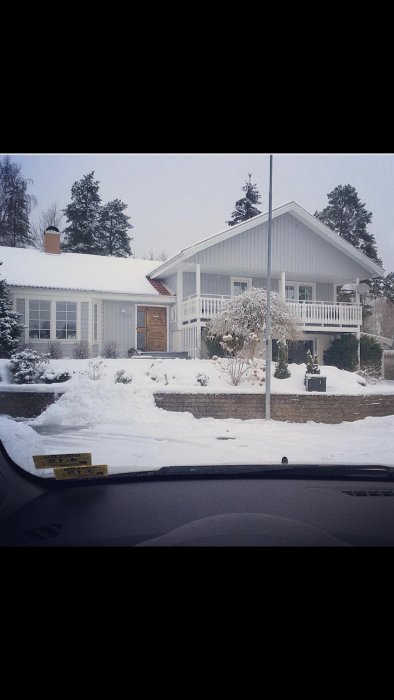 Vit villa med snöbeklätt tak och en snötäckt trädgård, med planer på taklyft för att matcha övre våningen.