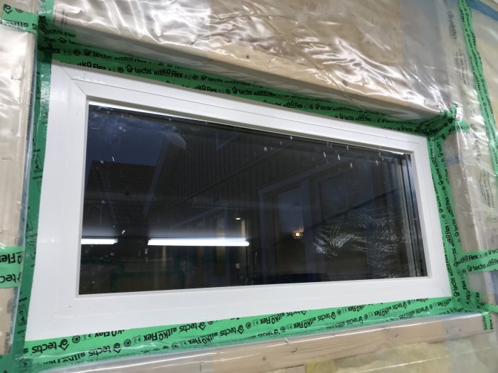 Fönster installerat med tätningsband på karmen, skyddad med plast, redo för smygmontering.